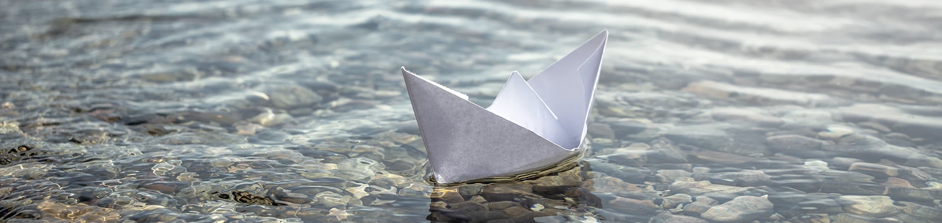 Weißes Papierboot schwimmt auf ruhigem Wasser